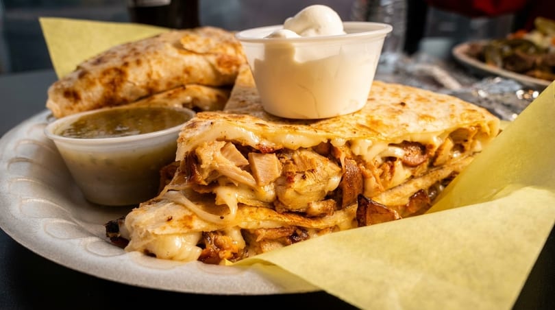 Chicken quesadilla with melted cheese, salsa verde, and sour cream on a white plate.
