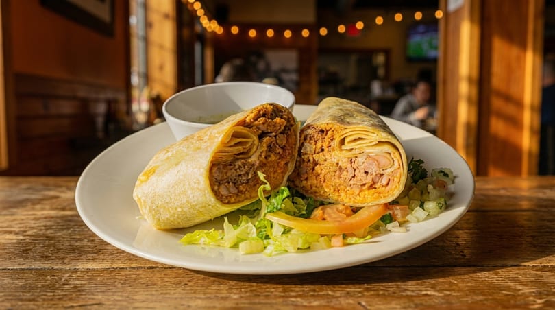 A large burrito, cut in half, served on a white plate with lettuce and salsa.