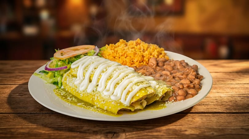Steaming green enchiladas topped with sour cream and cheese, served with rice, beans, and salad.